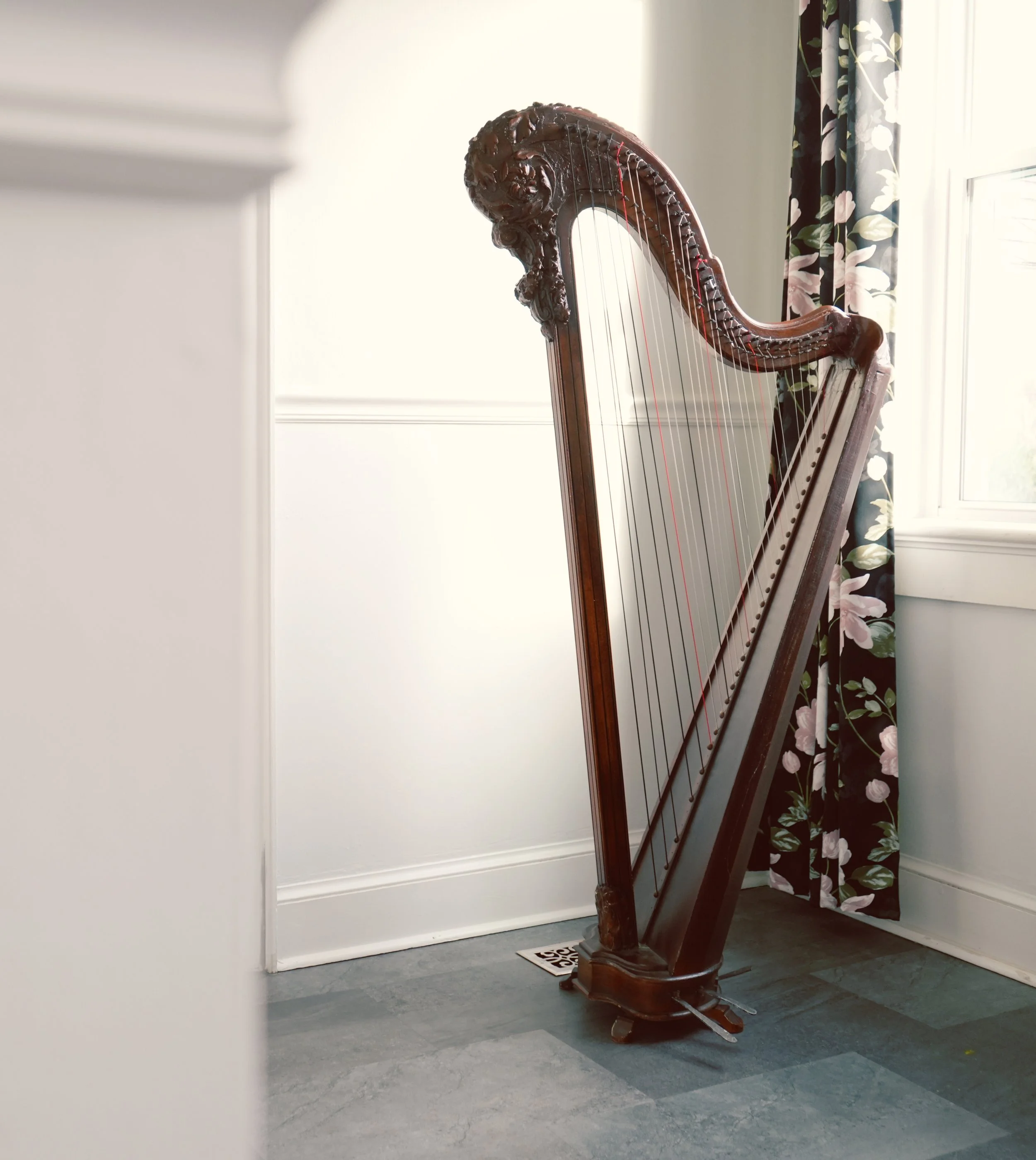 An antique wooden harp in the Erard style standing in a room near a window.